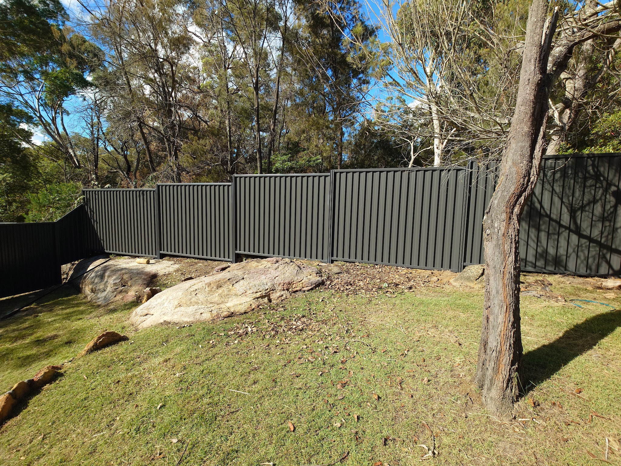 Charcoal steel panel fence along a sloping bush block