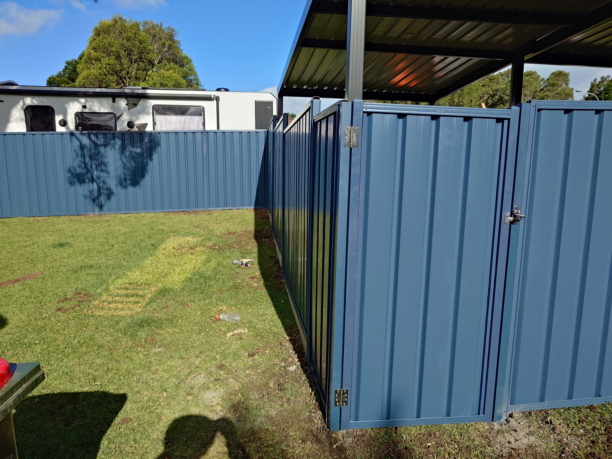 Blue-grey steel panel fence and matching gate beside a carport